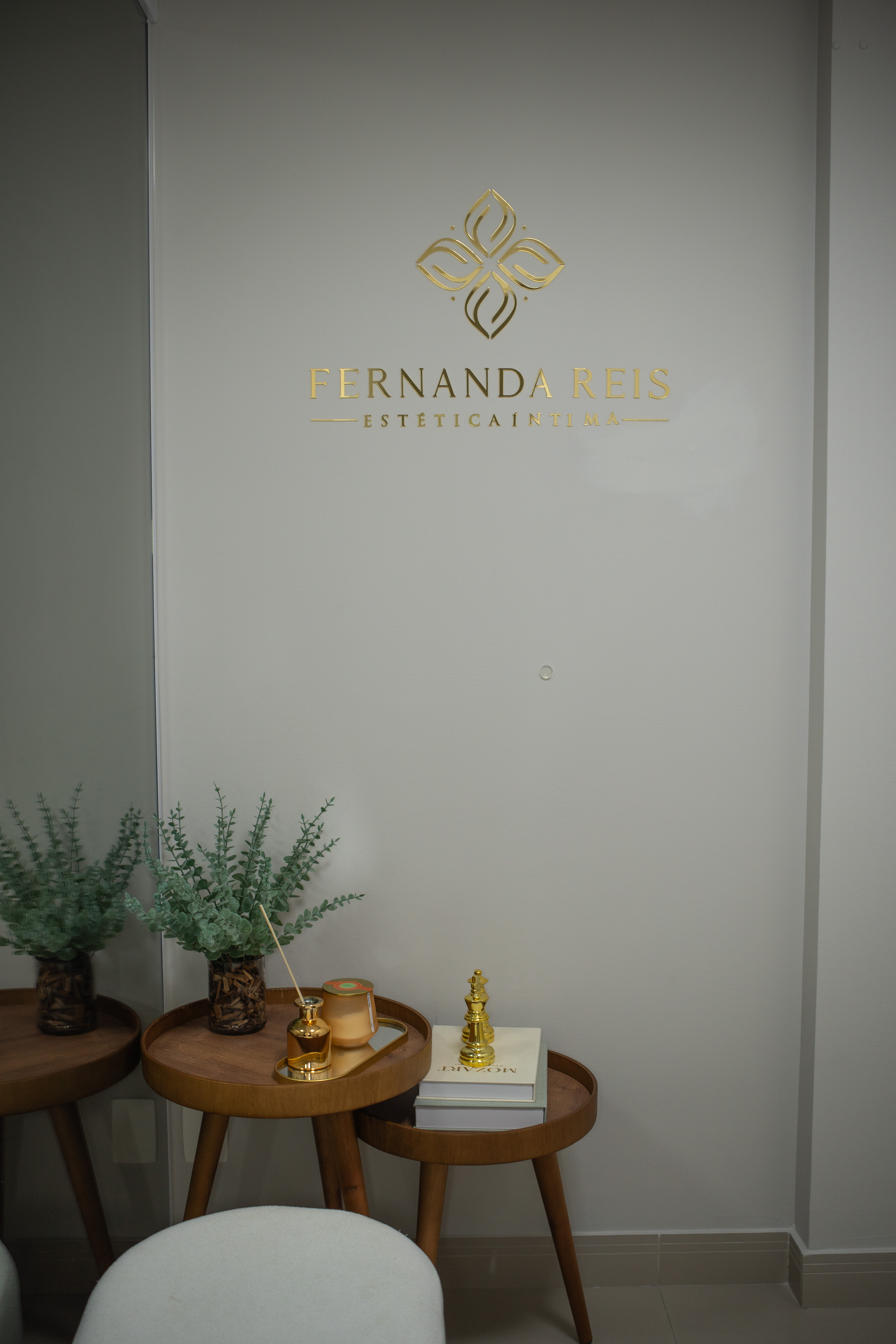 Espaço da clínica Fernanda Reis Estética Íntima, com logotipo dourado, plantas e mesas decorativas